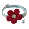 A red knitted floral dog collar with a light blue patterned strap and a silver rhinestone bell.