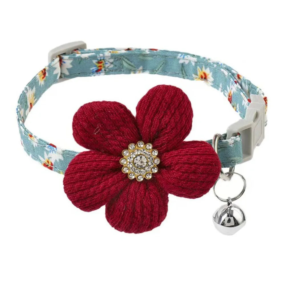 A red knitted floral dog collar with a light blue patterned strap and a silver rhinestone bell.