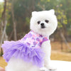 Un chien blanc portant une robe en mousseline de dentelle florale violette à volants.