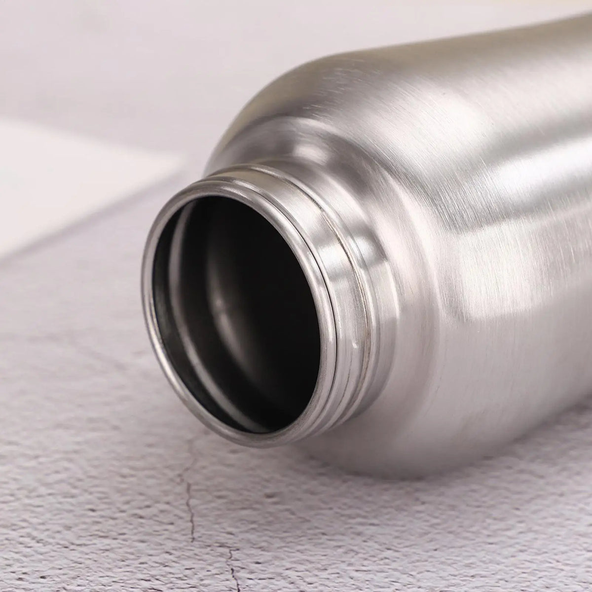 A close-up view of a silver portable leak-proof dog water bottle with an open built-in bowl.
