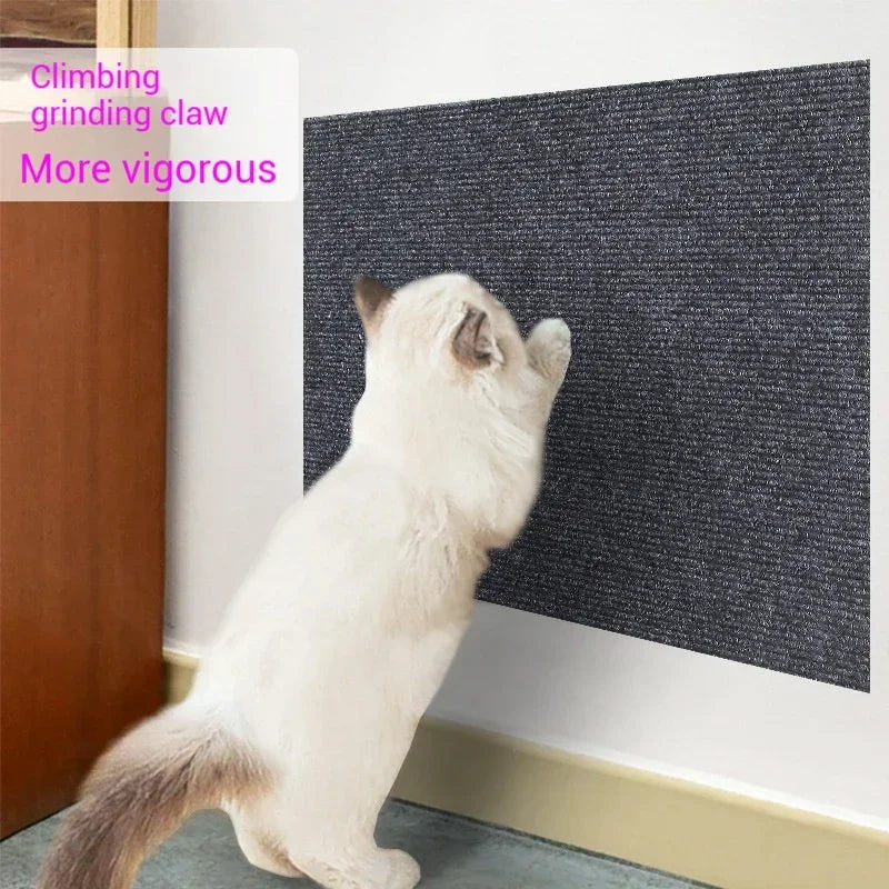A white cat is using a climbing grinding claw on a dark gray scratching mat placed against a wooden cabinet.