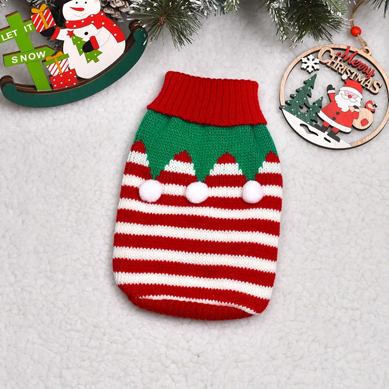 A knitted red and white striped winter dog sweater with green trim and white pom-poms, displayed on a light background.