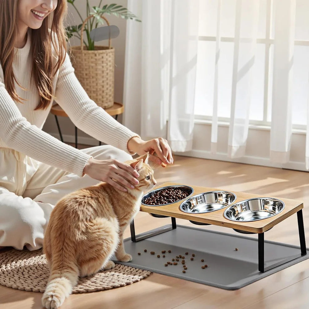 A woman feeds a cat using an elevated bowl stand with a waterproof anti-slip feeding mat on a wooden floor.