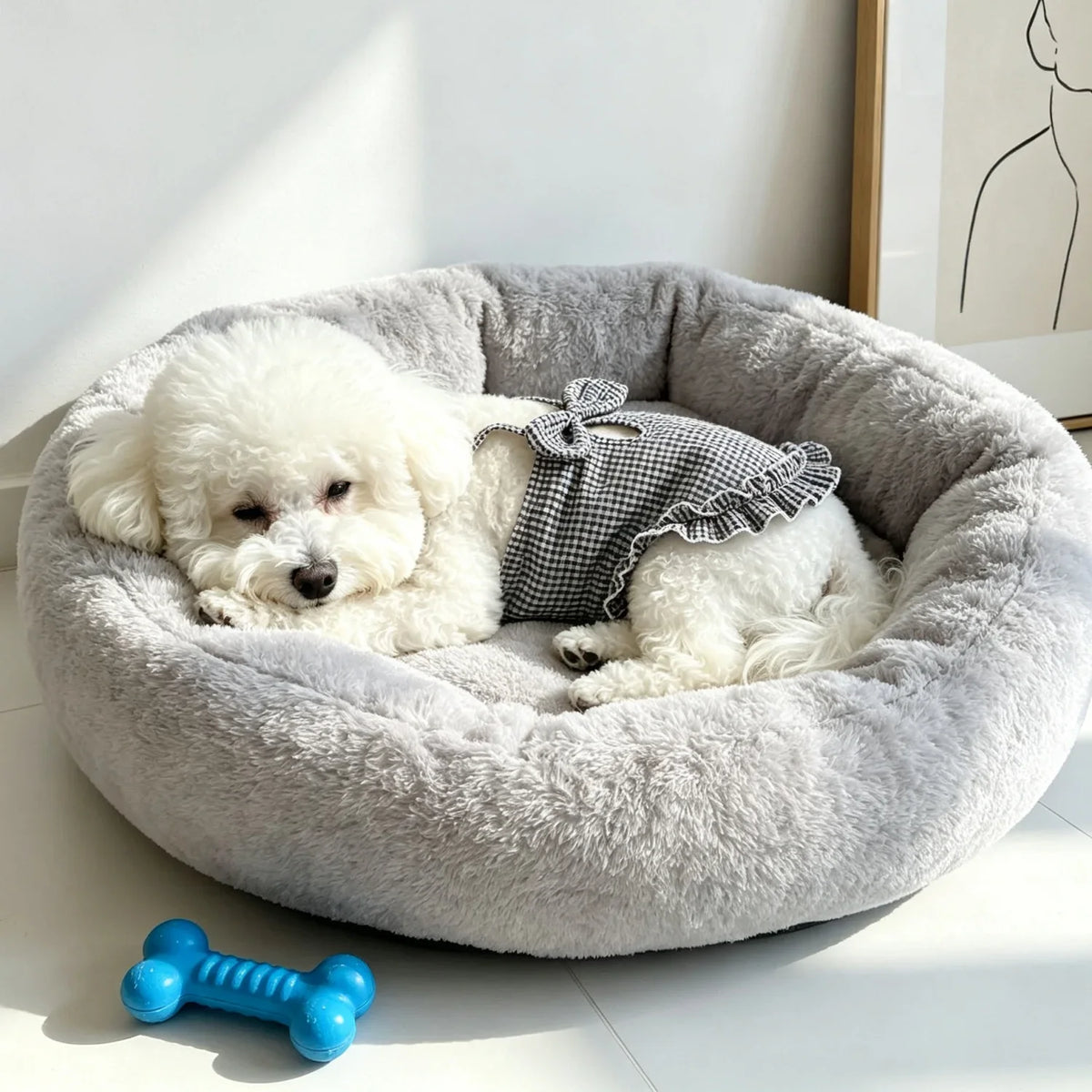 A fluffy white dog is lying inside a gray pet bed with a black and white checkered fabric.