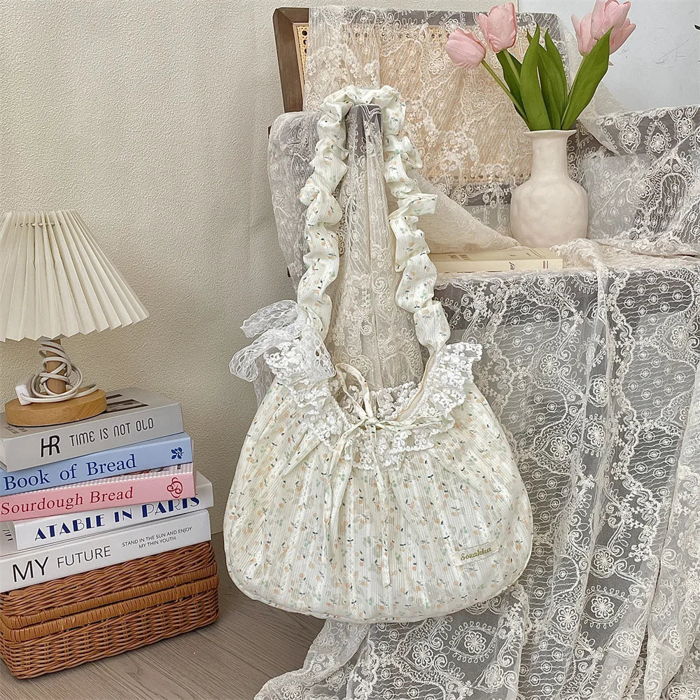 A white floral lace bowknot shoulder bag with a pleated design displayed on a lace tablecloth.
