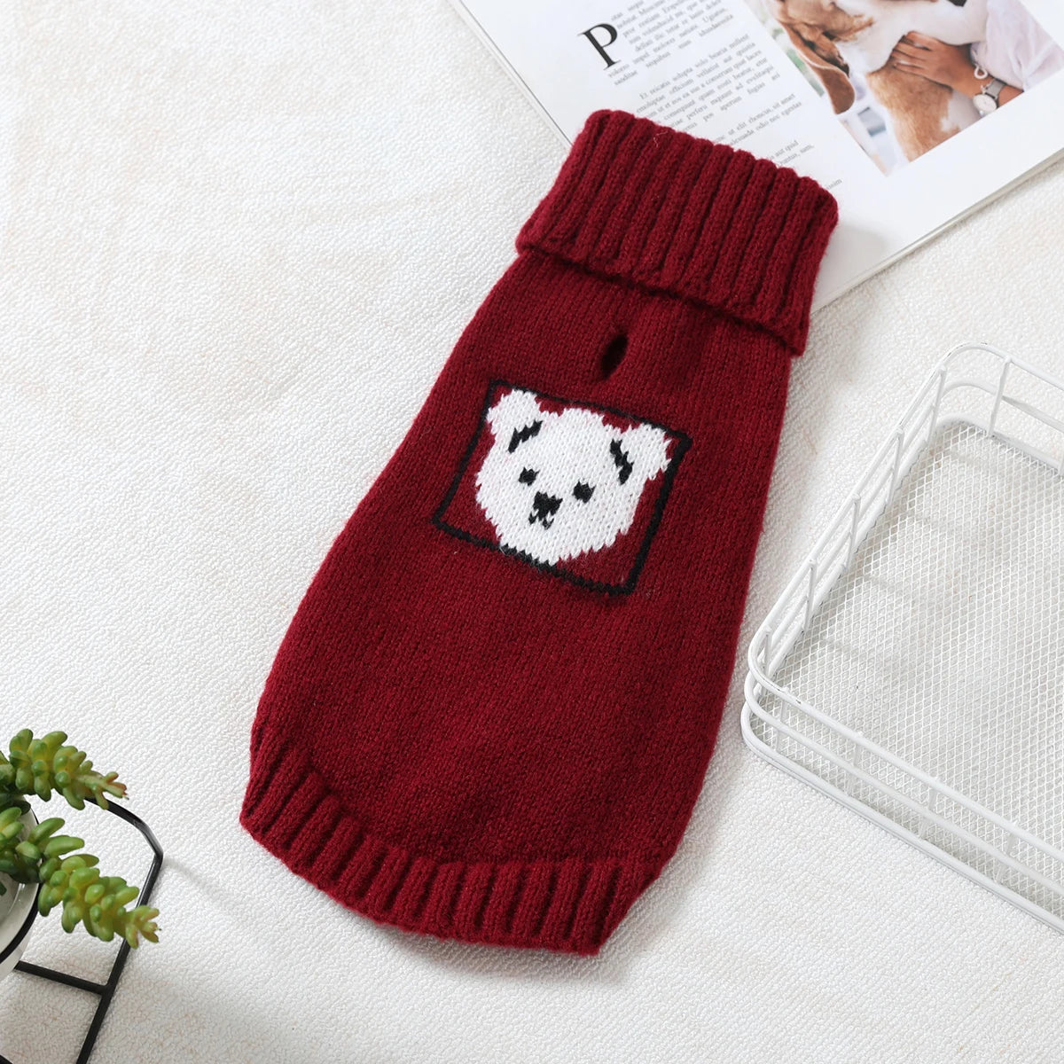 A deep red knitted sweater with a white bear design for a small to medium dog is displayed on a white surface.