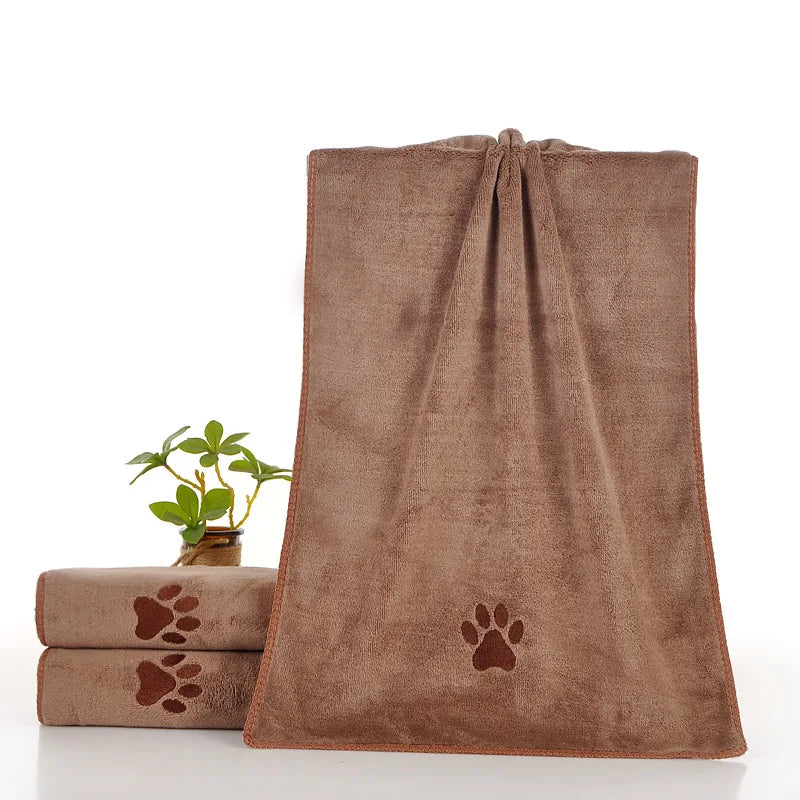 A brown pet bath towel with a paw print design is displayed next to rolled towels.
