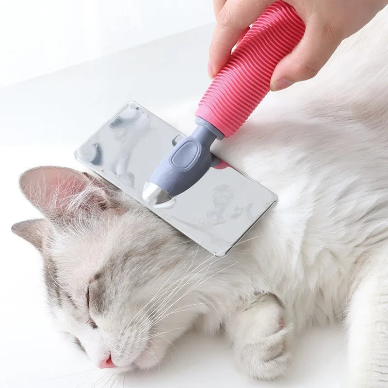 A hand is using a pink silicone cat comb with stainless steel pins to gently groom a sleeping white and gray cat.