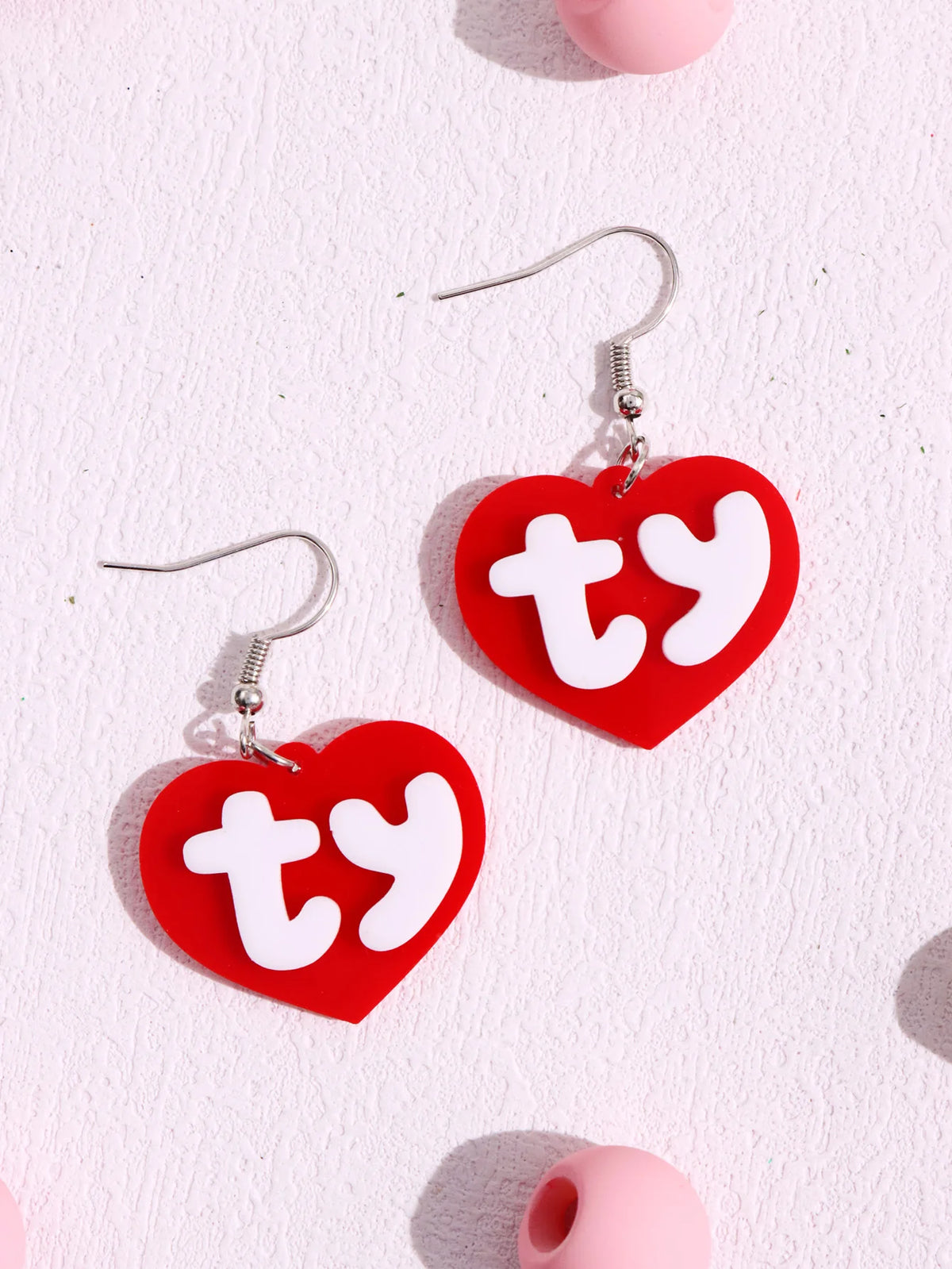 A pair of red acrylic heart stud earrings with white initial letters on silver ear wires.