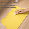 A hand wipes a yellow silicone cat face pet feeding mat with a wipe to clean it.