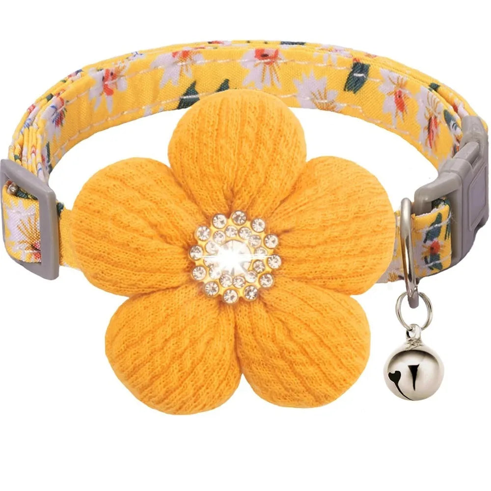 A yellow knitted floral dog collar with a large orange flower and a silver rhinestone bell.