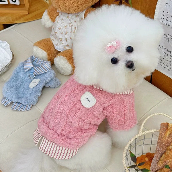 A fluffy white dog plush toy wearing a pink knitted hoodie with white trim and striped hem.