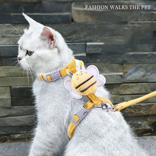 A white cat wearing a yellow and purple cartoon bee harness and leash set.