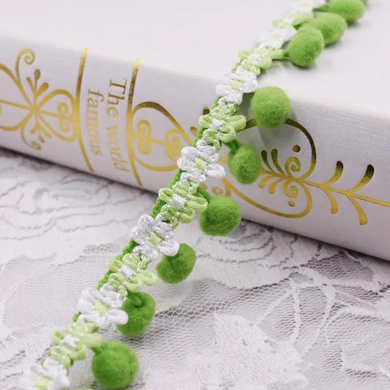 Lace trim featuring white floral embroidery and bright green pom poms on a white background.