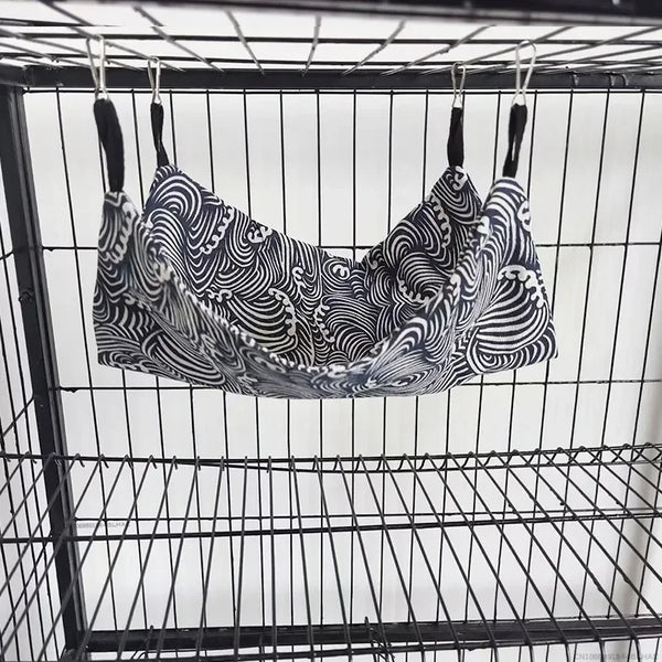 A double-layer plush hamster hammock with a black and white swirling pattern hanging inside a wire cage.