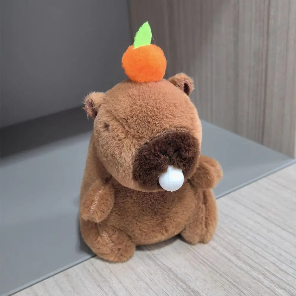 Braunes Capybara-Plüschtier mit orangefarbenen Ohren und grünen Flügeln auf einer hellen Holzoberfläche.