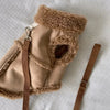 A tan, fluffy dog vest with a brown leather strap is shown on a white background.
