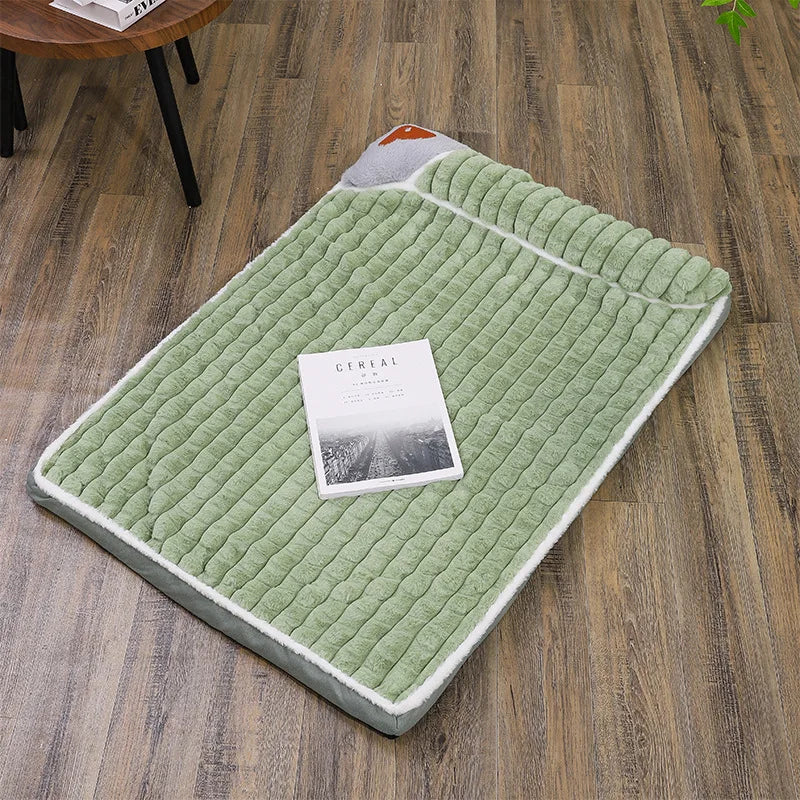 Un lit pour chien matelassé vert clair avec une housse amovible et une petite carte posée dessus, sur un plancher en bois.
