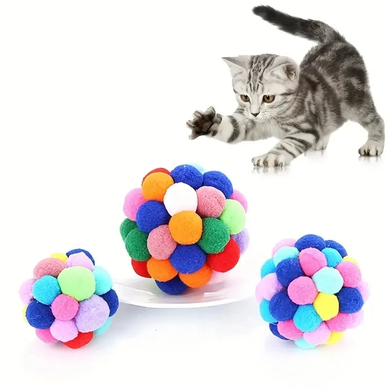 Grauer Kätzchen spielt mit einem bunten, flauschigen Ballspielzeugset.