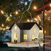مصباح طعام للطيور خارجي شمسي بتصميم منزل معلق بسلك معدني على عمود داكن.