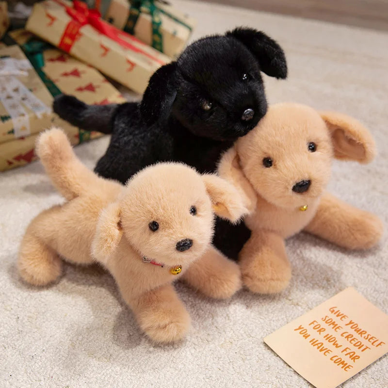 Three plush dog toys, including a black puppy and two light tan puppies, resting on a white surface.