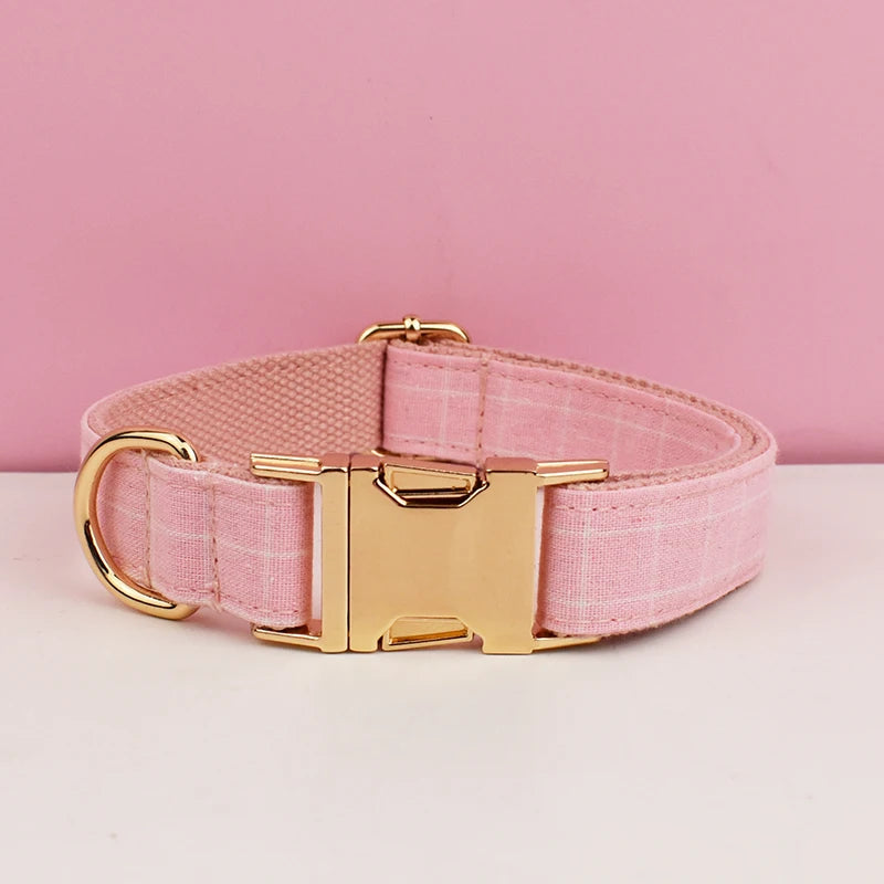 A pink plaid dog collar with a gold buckle is displayed on a white surface.