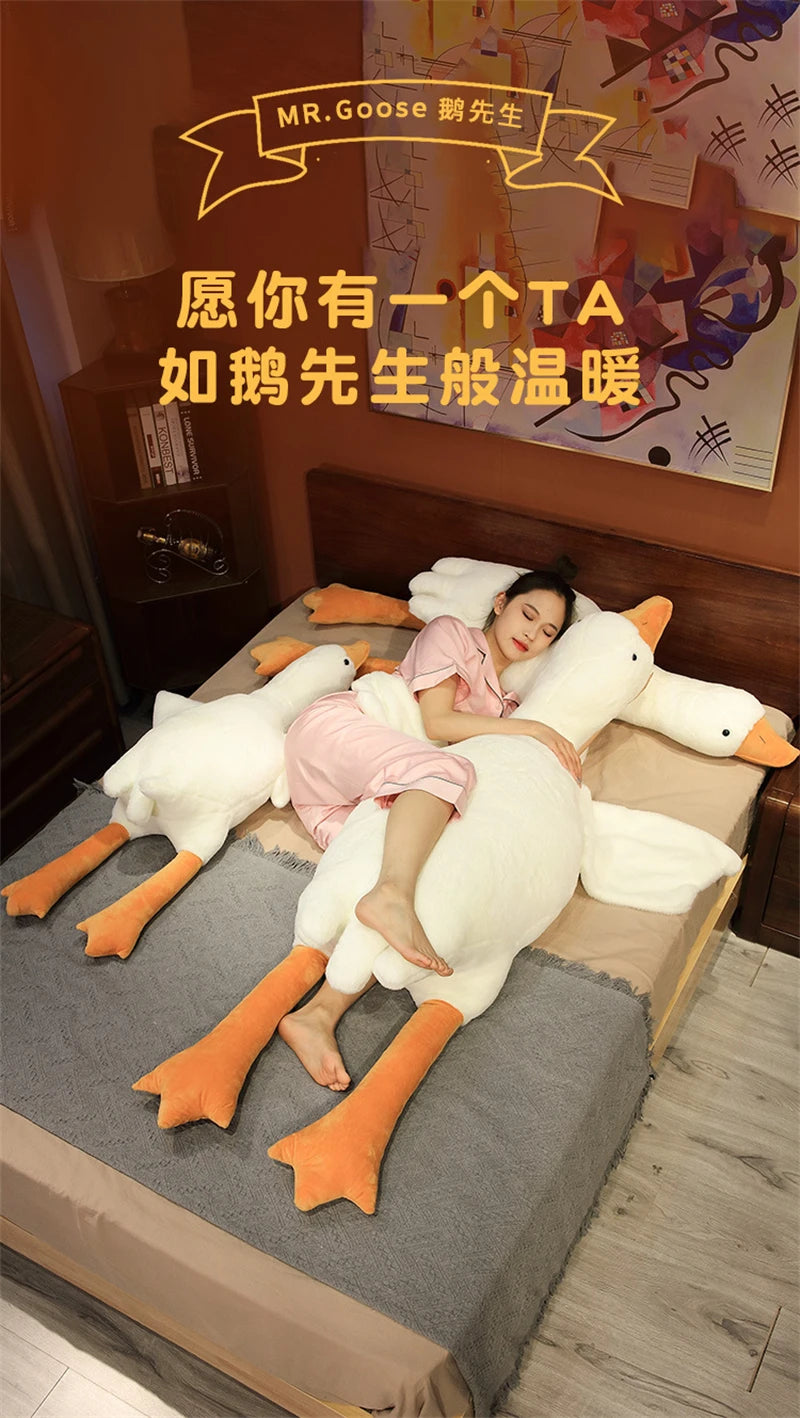 A person is relaxing on a bed with a large white plush goose body pillow, suggesting comfort and cuddling.
