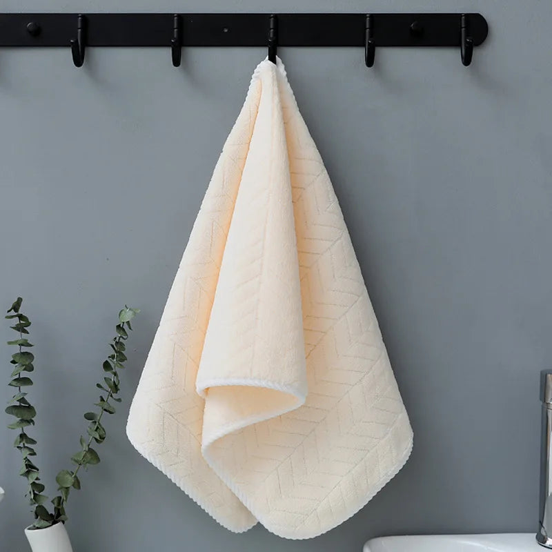 A fluffy, pale peach bath towel is hanging on a black rack against a gray wall.
