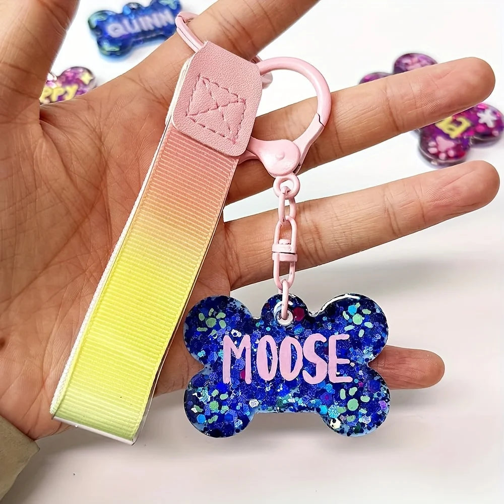 A pink silicone dog bone charm with a blue glitter tag is held in a hand.