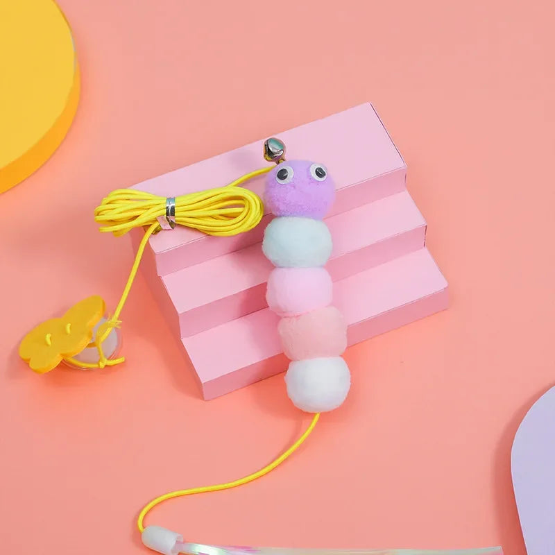 A purple and light blue hanging cat toy with a yellow rope is displayed on a pink background.