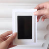 A hand is holding a white frame containing a black print, likely for pet paw print and handprint supplies.