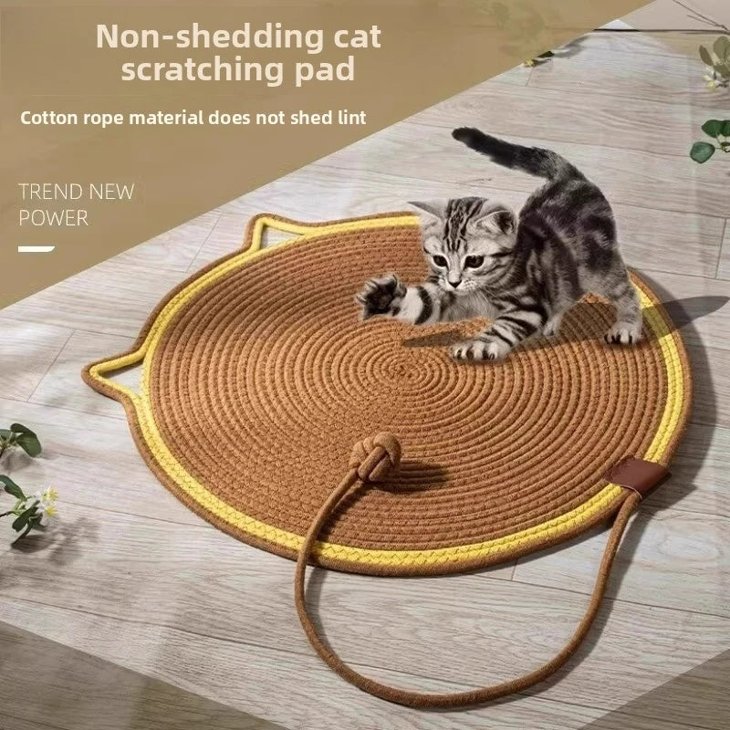 A brown cat is playing on a round, woven scratching pad with a yellow edge and a leather strap.