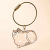 A clear glass charm shaped like a cat is suspended from a braided gold-colored cord with a metal clasp.
