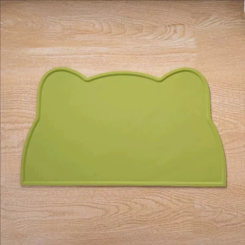 A light green silicone mat shaped like a cat face used as a pet feeding mat for food and water bowls.