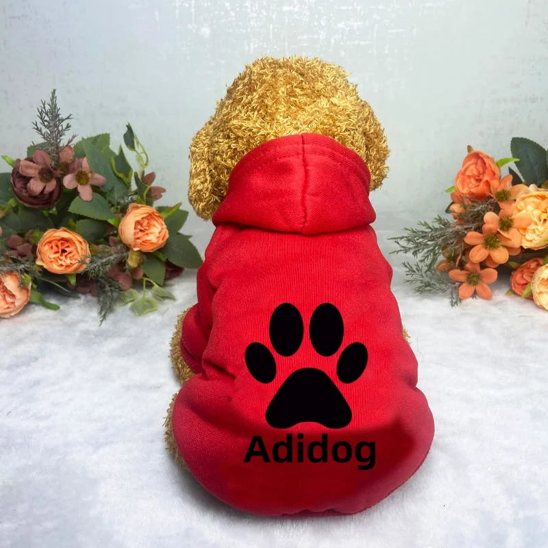 A red cotton dog hoodie sweatshirt with a black paw print design and a gold fluffy hood resting on a white surface.