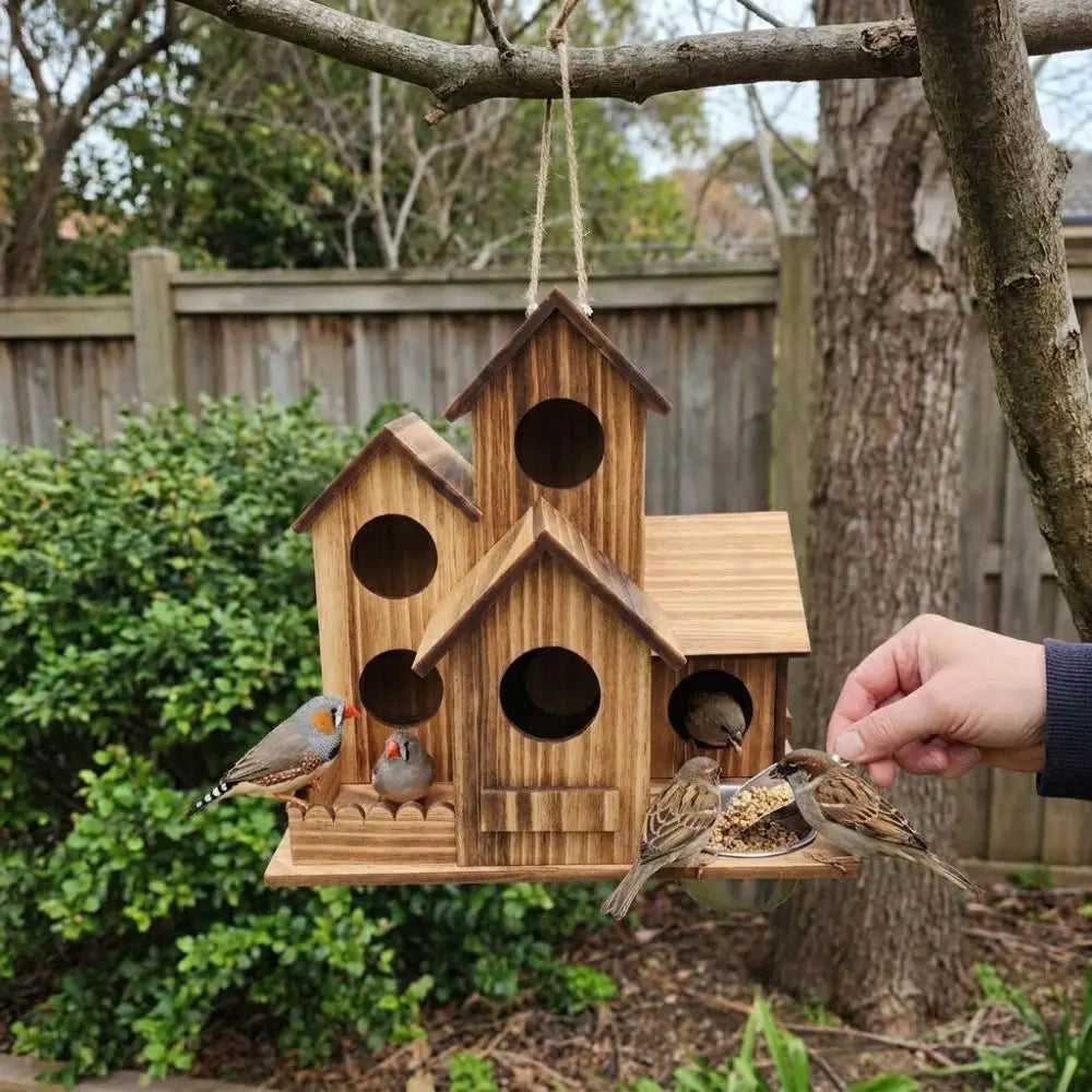 A handcrafted wooden bird house feeder with multiple entrances hangs from a branch in an outdoor setting.