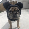 Un perro de color cría vistiendo un gorro de invierno de forro negro con orejas caídas, parado al aire libre.