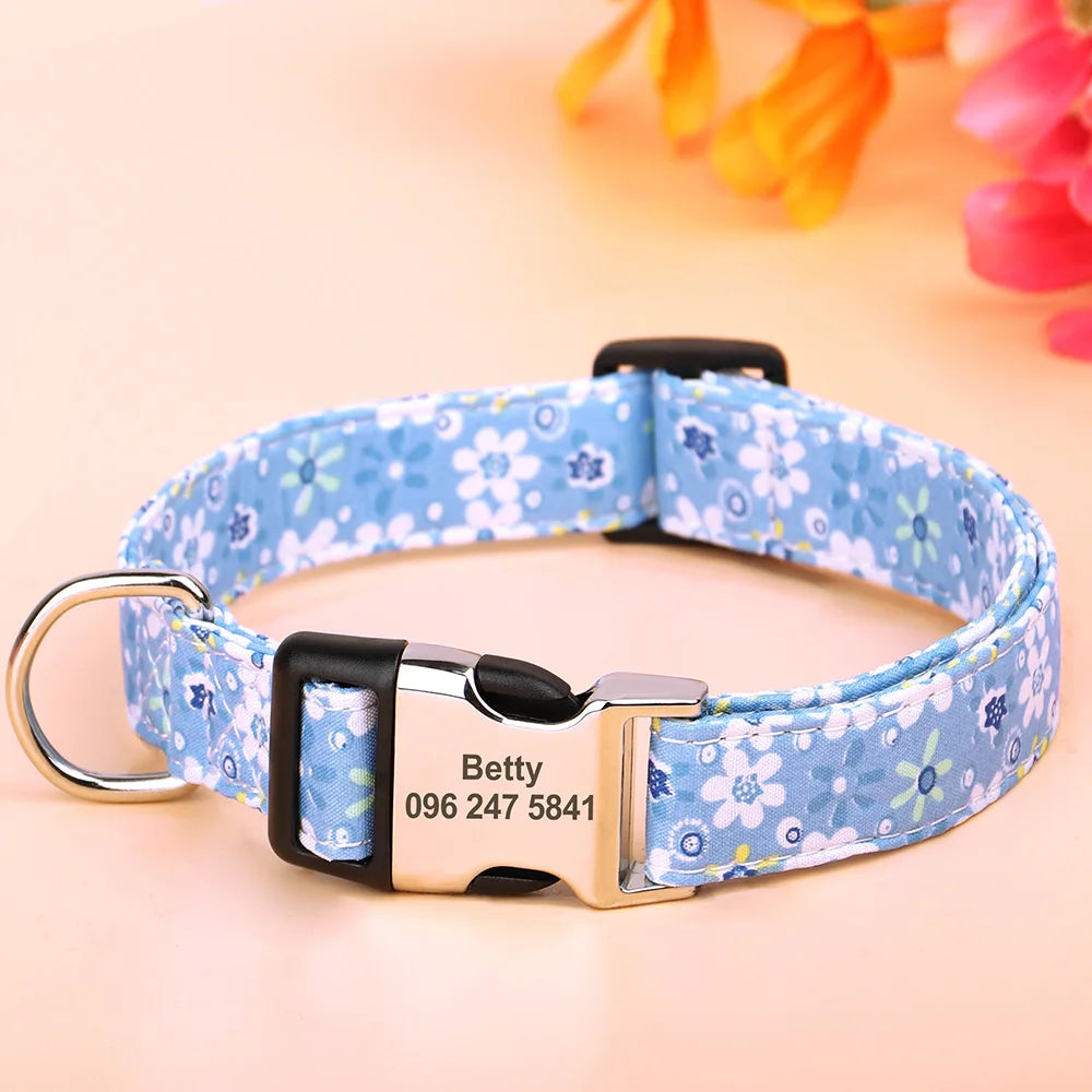 A light blue floral print dog collar with a silver buckle and an engraved name tag on a wooden surface.
