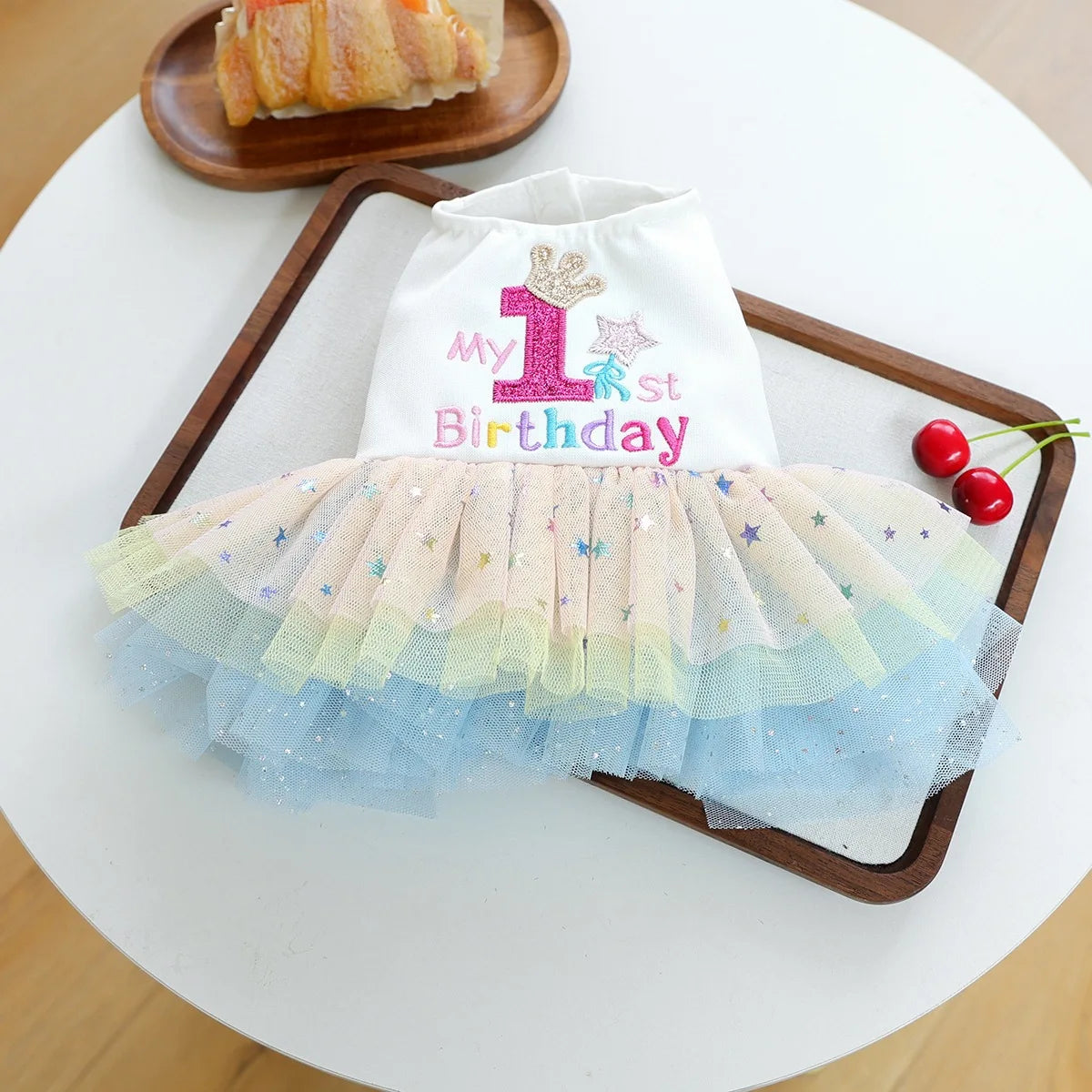 A white and pink elegant dog birthday suit with a crown design displayed on a wooden tray.