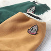 A close-up of a tan knitted sweater with an embroidered emblem on the sleeve, resting on a green and white fuzzy garment.