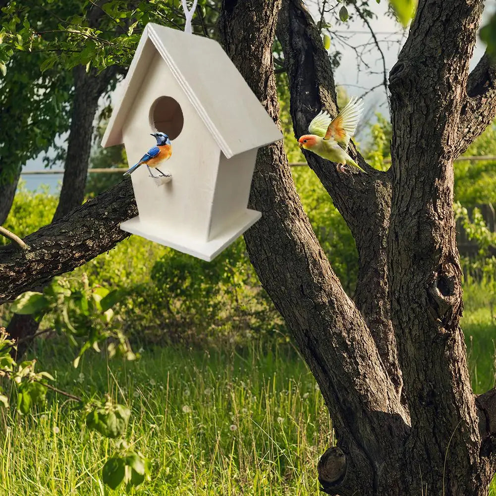A white wooden wall-mounted bird house is nestled in a tree branch with a blue bird perched inside.