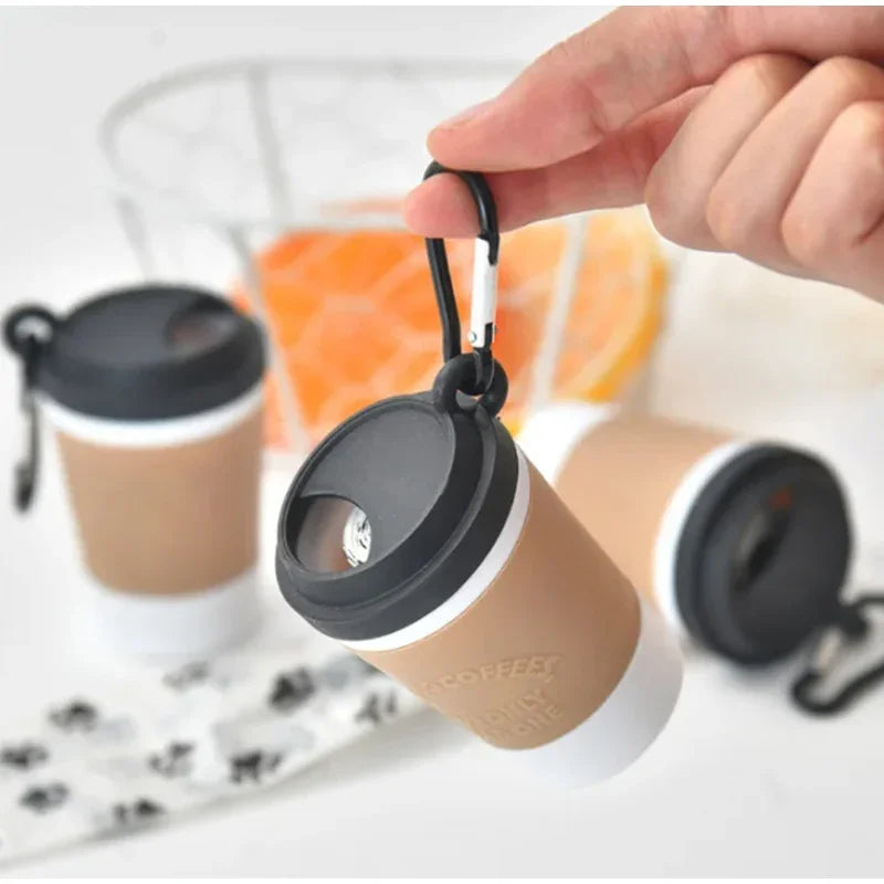 A hand is holding a portable pet poop trash can dispenser with a beige body and black lid.
