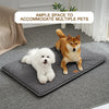 A fluffy white dog is resting on a gray quilted mat indoors.