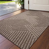 A rectangular gray textured doormat with a geometric pattern placed on a wooden floor near a white door.
