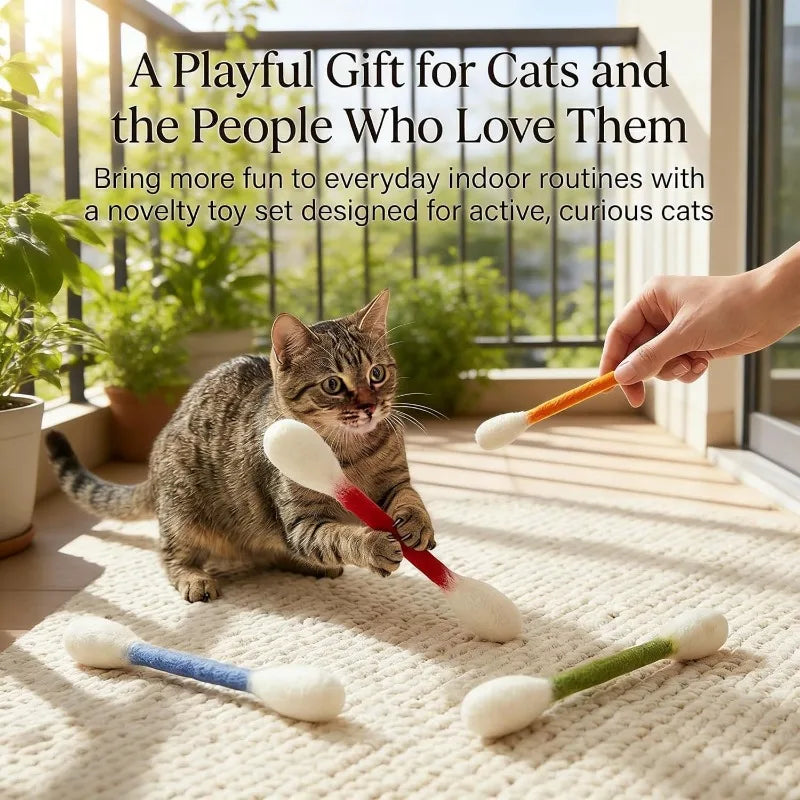 A hand is holding a catnip wand toy with various colored foam balls and rope, lying on a light-colored rug.