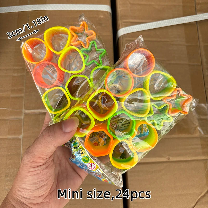 A hand holds a clear plastic bag containing 24 colorful spring coil toys in various shapes and colors.