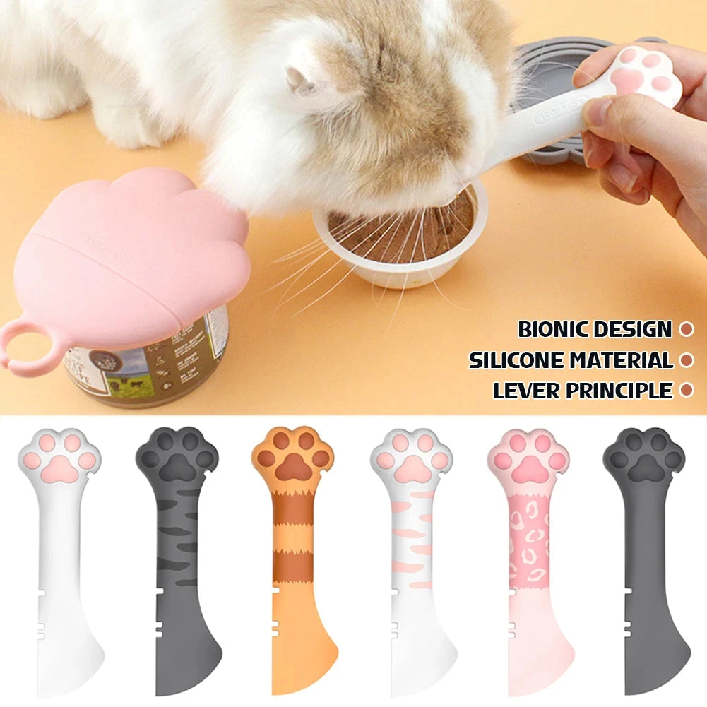A hand is using a pink silicone cat paw tool to scoop food from a can, shown alongside various colored and shaped silicone pa