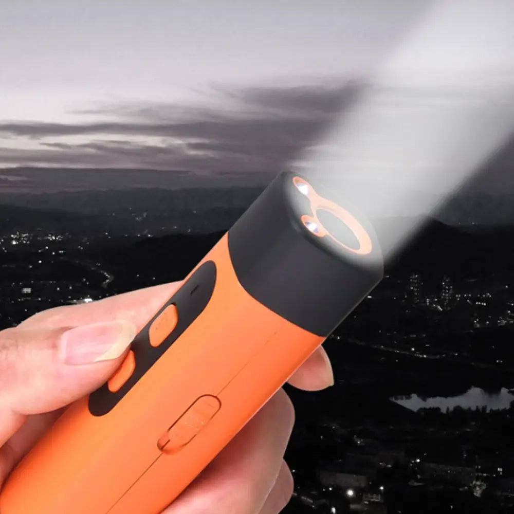 A hand holds an orange ultrasonic dog repeller with an LED flash light, emitting a bright beam against a dark landscape.