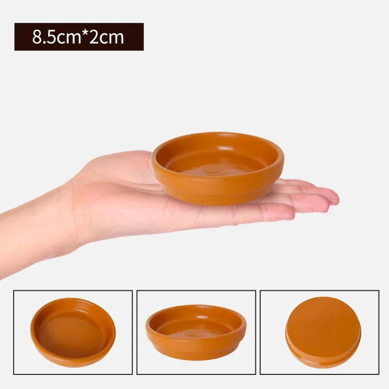 A hand holds a small, round, terracotta-colored ceramic aquarium breeding cave or shrimp shelter.
