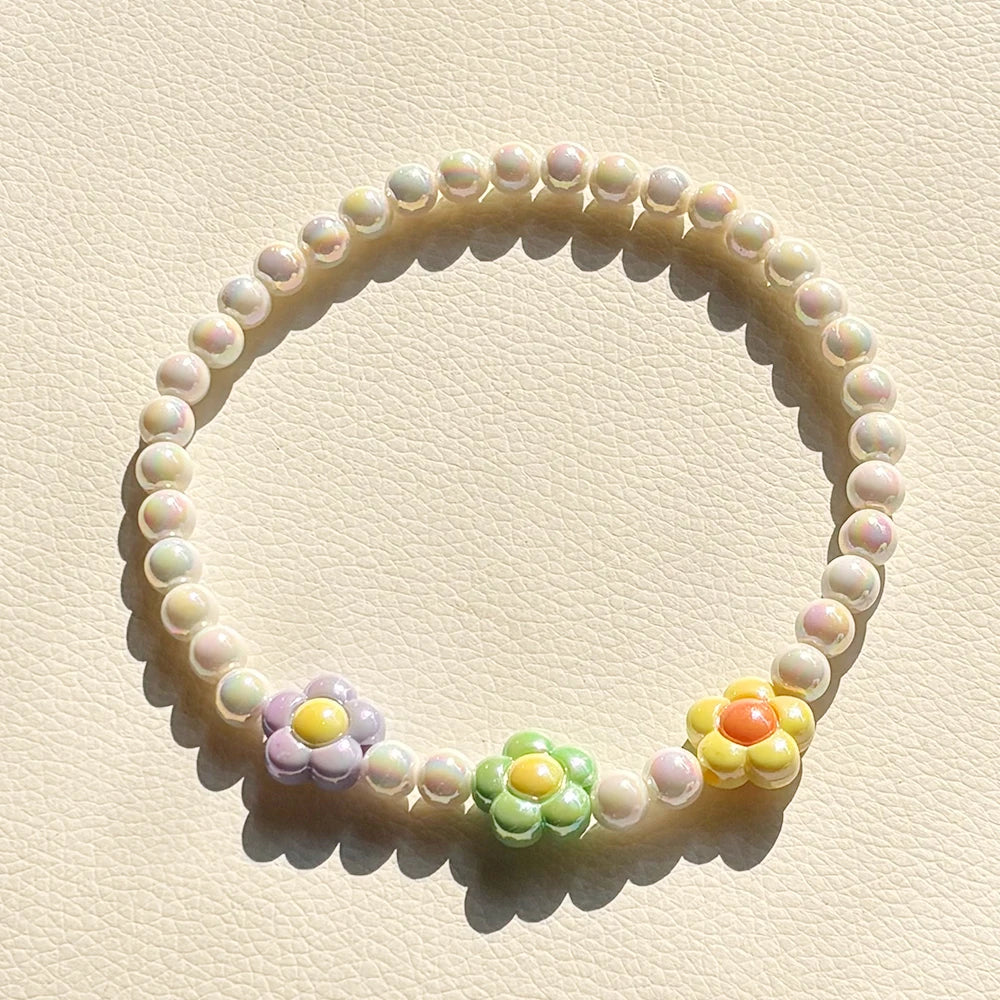 A circular necklace made of pastel floral beads, featuring soft pink, yellow, and green tones.